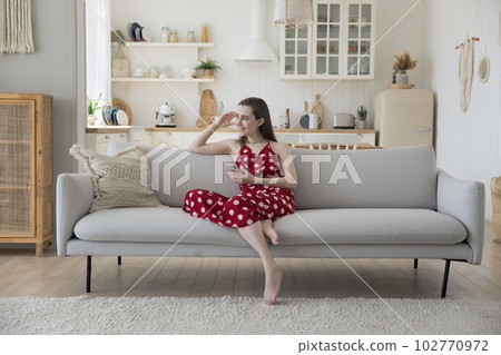 Happy thoughtful girl with smartphone sitting on comfortable home sofa, Happy thoughtful girl with smartphone sitting on comfortable home sofa, 102770972