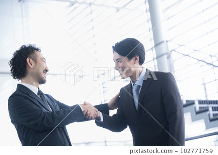 兩名穿西裝的男性員工微笑著握手 一名 40 多歲的男子和一名 20 多歲和 30 多歲的男子拍拍肩膀 102771759