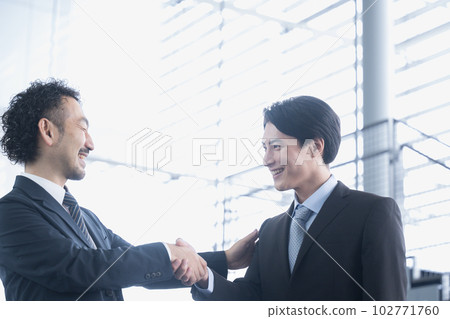 兩名穿西裝的男性員工微笑著握手 一名 40 多歲的男子和一名 20 多歲和 30 多歲的男子拍拍肩膀 102771760