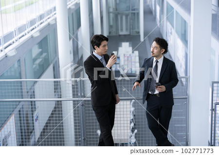 鳥瞰兩個穿著西裝的男人在走廊裡邊喝咖啡邊聊天。帶複製空間 鳥瞰兩個穿著西裝的男人在走廊裡邊喝咖啡邊聊天。帶複製空間 102771773