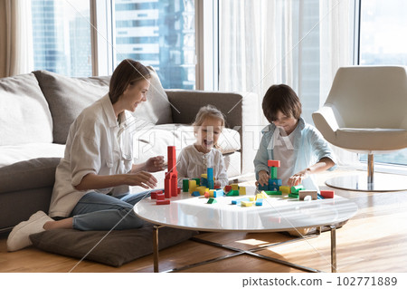Happy mother helping little sibling kids to build toy towers Happy mother helping little sibling kids to build toy towers 102771889