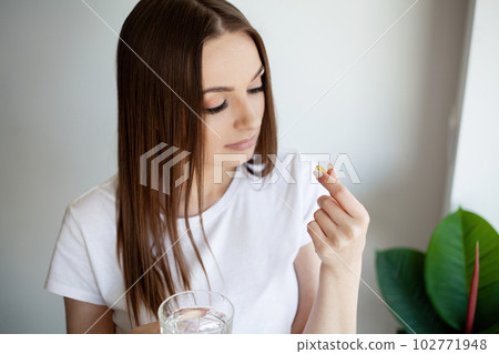 Beautiful woman holding capsule with a fish oil source of Omega-3 fatty acids Beautiful woman holding capsule with a fish oil source of Omega-3 fatty acids 102771948