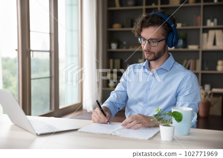 Serious young adult student man in wireless headset watching webinar 102771969
