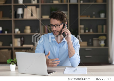 Serious freelance business man talking on mobile phone at home Serious freelance business man talking on mobile phone at home 102772072