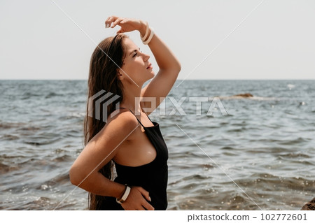 Woman summer travel sea. Happy tourist in hat enjoy taking picture outdoors for memories. Woman traveler posing on the beach at sea surrounded by volcanic mountains, sharing travel adventure journey 102772601