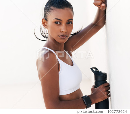 Portrait of a confident female athlete in a white sports bra and holding a black bottle Portrait of a confident female athlete in a white sports bra and holding a black bottle 102772624
