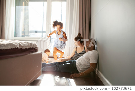 Snapshot of diverse family playing with happy children on floor at home run around in motion, authentic family life, unposed, spontaneous moments of fun and laughter 102773671