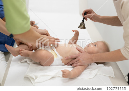 Baby beeing vaccinated by pediatrician in presence of his mother. Preventive vaccination against Diphtheria, whooping cough, tetanus, hepatitis, haemophilus influenzae, pneumococcus, poliomyelitis. 102775535