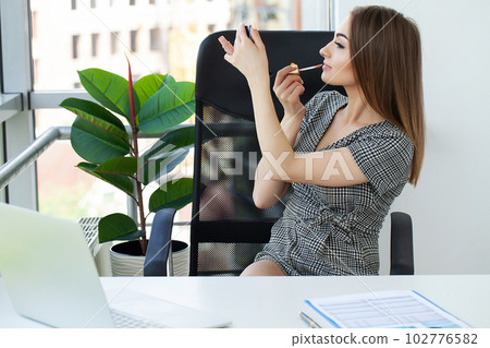 Pretty happy businesswoman doing make up in office 102776582