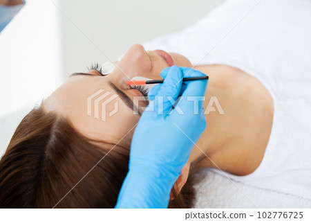 Eyelash extension procedure, master fake long lashes beautiful female eyes. 102776725