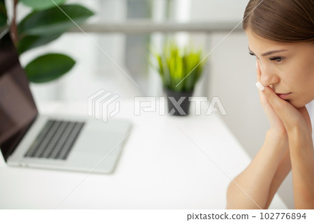 Woman suffering from toothache and touching her cheek while sitting at her desk Woman suffering from toothache and touching her cheek while sitting at her desk 102776894