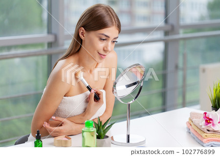 Woman sitting by the mirror and applying makeup 102776899