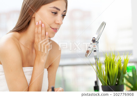 Woman sitting by the mirror and applying makeup Woman sitting by the mirror and applying makeup 102776908