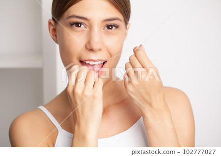Woman using dental floss for cleaning her teeth Woman using dental floss for cleaning her teeth 102777027