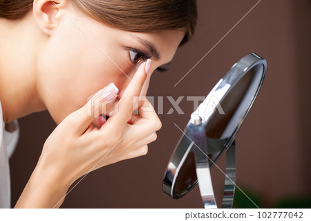 Young woman putting contact lens in her eye, close up Young woman putting contact lens in her eye, close up 102777042