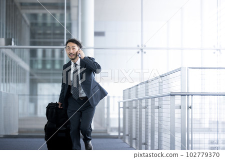 A man in his 40s wearing a middle suit running while calling at the airport or train station Copy space A man in his 40s wearing a middle suit running while calling at the airport or train station Copy space 102779370