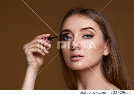 young woman applying black mascara on long thick eyelashes young woman applying black mascara on long thick eyelashes 102779663