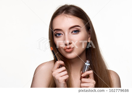 beautiful young woman with pouted lips holding lip gloss 102779686