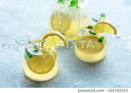 Lemonade with mint. Lemon water drink with ice. Two glasses and a pitcher Lemonade with mint. Lemon water drink with ice. Two glasses and a pitcher 102782025
