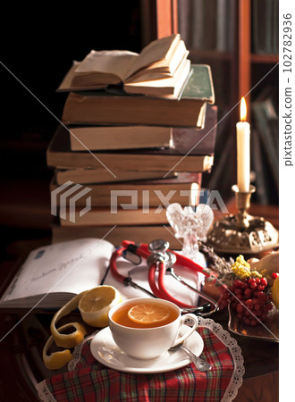 medical still life. A stack of vintage books, a phonendoscope, a cup of tea with lemon, an open notepad, medicinal plants on a wooden table medical still life. A stack of vintage books, a phonendoscope, a cup of tea with lemon, an open notepad, medicinal plants on a wooden table 102782936