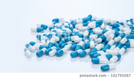 Pile of blue and white capsule pills. Pharmacy product. Prescription drug. Healthcare and medicine. Pharmaceutical industry. Pharmaceutical science. Prescription medication. Capsule pill production. 102785087