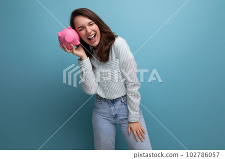cute 20s brunette lady in shirt and jeans saved up her money for a dream in a piggy bank cute 20s brunette lady in shirt and jeans saved up her money for a dream in a piggy bank 102786057