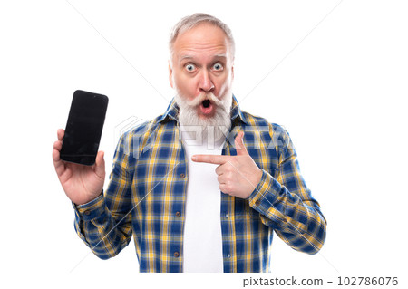 surprised senior pensioner gray-haired man with a beard in a shirt holding a smartphone on a white surprised senior pensioner gray-haired man with a beard in a shirt holding a smartphone on a white 102786076