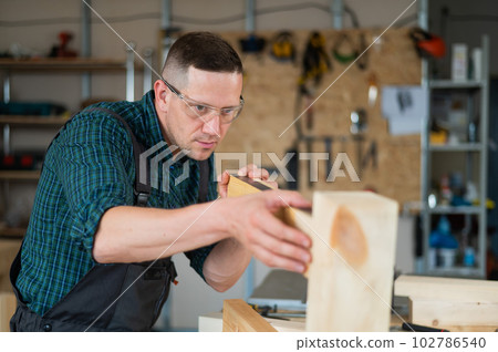Carpenter measures wooden planks in the workshop. Carpenter measures wooden planks in the workshop. 102786540