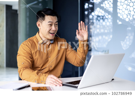 Happy and successful asian boss talking with colleagues on video call, using laptop, waving hands greeting to camera, businessman at work Happy and successful asian boss talking with colleagues on video call, using laptop, waving hands greeting to camera, businessman at work 102786949