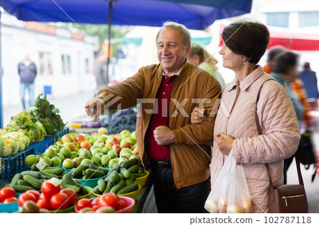 Aged man and woman customers buying vegetables in open-air market Aged man and woman customers buying vegetables in open-air market 102787118