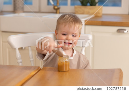 Happy family at home. Baby boy feeding himself in kitchen. Little boy with messy funny face eats healthy food. Child learns eat by himself holding spoon. Self feeding 102787236