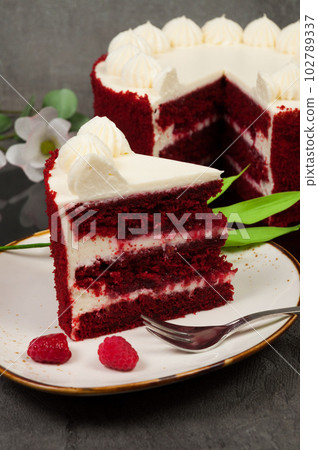 a piece of red velvet cake decorated with raspberries on a light plate 102789337