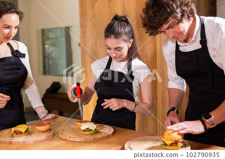 Preparing delicious burgers. Chef cooking meat burgers with beef, cheese and vegetables. Close-up Preparing delicious burgers. Chef cooking meat burgers with beef, cheese and vegetables. Close-up 102790935