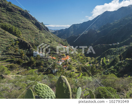 View over small village La Laja, red and white rural houses in lush green valley with palm trees. Landscape near national park Garajonay on La Gomera, Canary Islands, Spain. View over small village La Laja, red and white rural houses in lush green valley with palm trees. Landscape near national park Garajonay on La Gomera, Canary Islands, Spain. 102791049