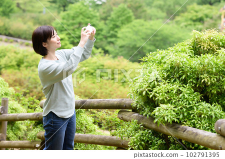 一位女士用智能手機相機為公園的綠地拍照 一位女士用智能手機相機為公園的綠地拍照 102791395