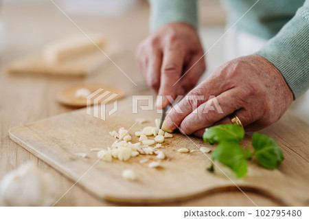 Close up of senior man cutting garlic. Close up of senior man cutting garlic. 102795480