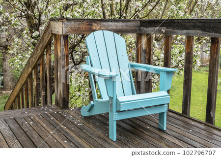 empty Adirondack chair on a wooden backyard deck, spring scenery with a blooming apple tree empty Adirondack chair on a wooden backyard deck, spring scenery with a blooming apple tree 102796707