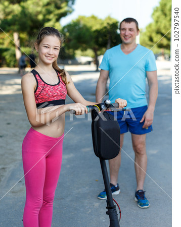 Girl riding kick scooter with father 102797540