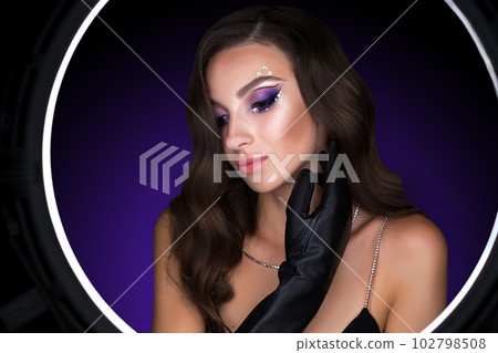 Female portrait of a young brunette girl with a beautiful evening make-up. The girl has gloves on her hands Female portrait of a young brunette girl with a beautiful evening make-up. The girl has gloves on her hands 102798508