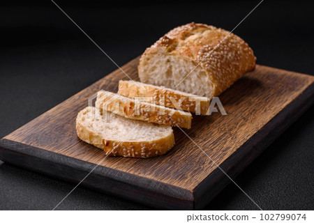 Crispy wheat flour baguette with sesame seeds on a wooden cutting board 102799074