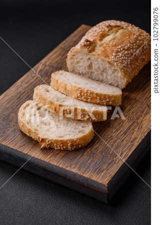 Crispy wheat flour baguette with sesame seeds on a wooden cutting board 102799076