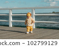 A toddler in a yellow jacket and pants walks on the pier 102799129