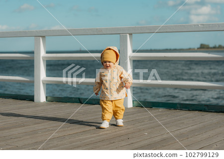 A toddler in a yellow jacket and pants walks on the pier 102799129