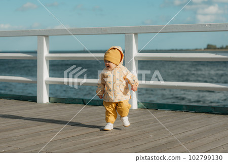 A toddler in a yellow jacket and pants walks on the pier 102799130