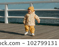 A toddler in a yellow jacket and pants walks on the pier 102799131