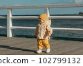A toddler in a yellow jacket and pants walks on the pier 102799132