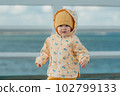A toddler in a yellow jacket and pants walks on the pier 102799133