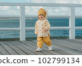 A toddler in a yellow jacket and pants walks on the pier 102799134