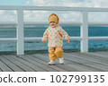 A toddler in a yellow jacket and pants walks on the pier 102799135