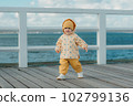 A toddler in a yellow jacket and pants walks on the pier 102799136